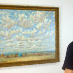 A viewer admiring André Hambourg’s 'Temps Doux à Deauville en Août' on a white gallery wall, appreciating its vibrant colors and impressionistic beach scene.