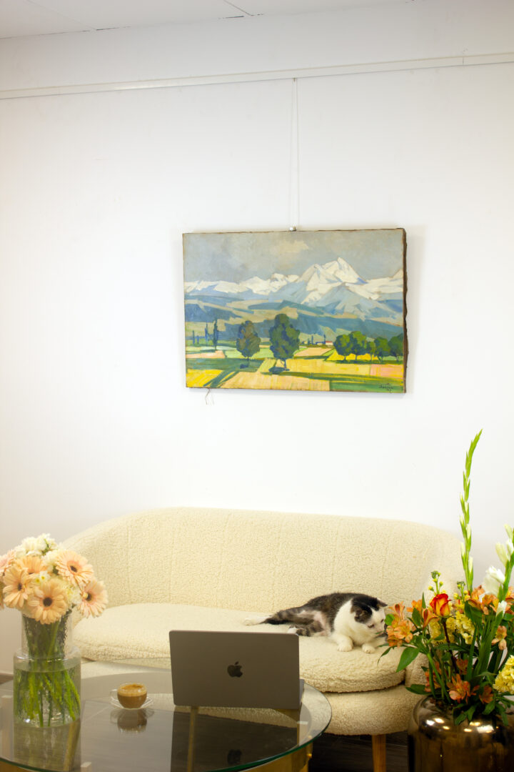 The painting 'Ararat Mountain' (1927) by Martiros Saryan displayed in an interior setting, hanging on a white wall above a beige sofa, with flowers and a laptop on a glass table.