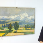 A person in a dark T-shirt observing 'Ararat Mountain' (1927) by Martiros Saryan, hanging unframed on a white wall.