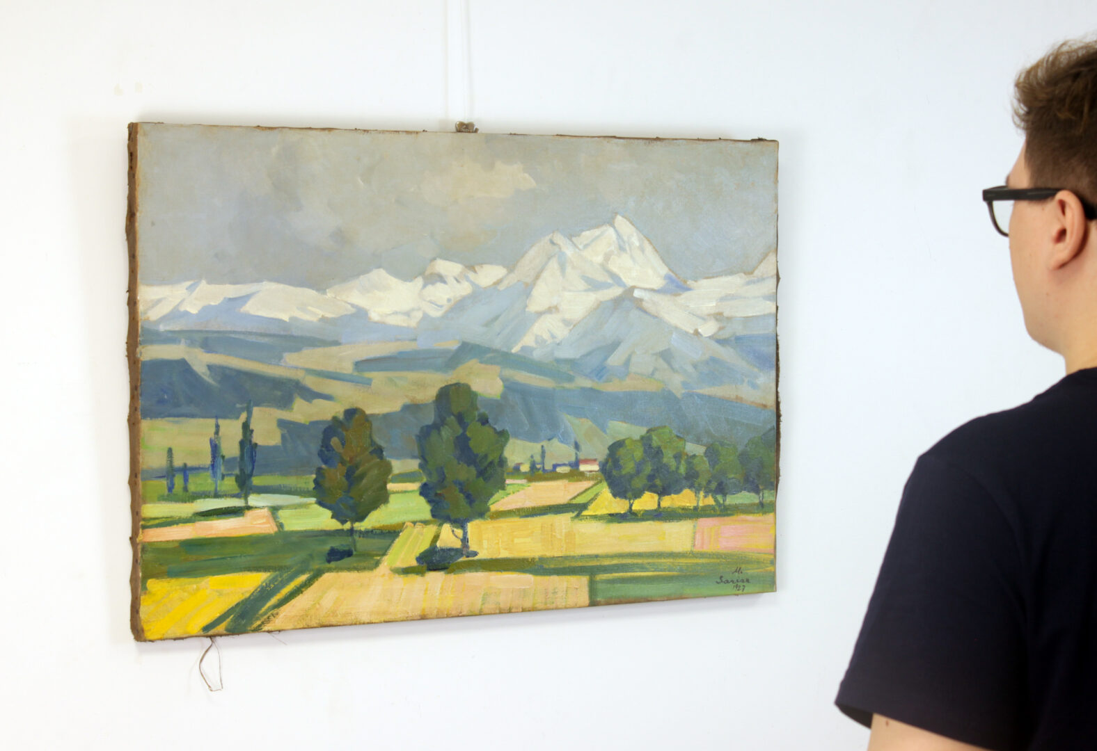 A person in a dark T-shirt observing 'Ararat Mountain' (1927) by Martiros Saryan, hanging unframed on a white wall.