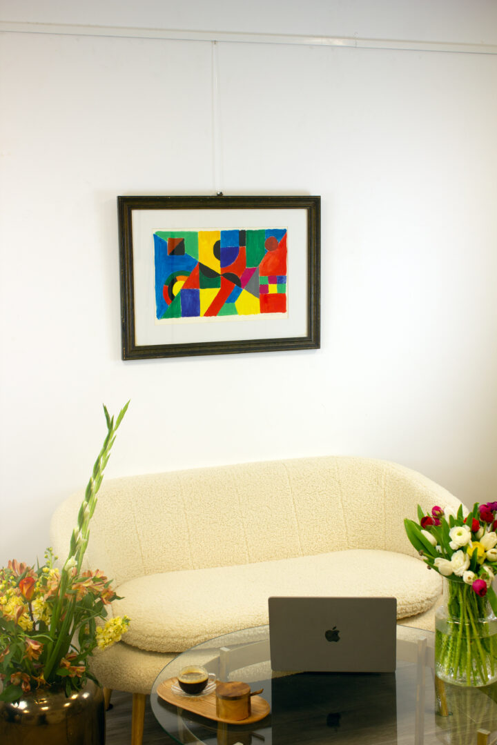 Rythme Couleur (1955) by Sonia Delaunay displayed on a gallery wall above a beige sofa with decorative flowers.