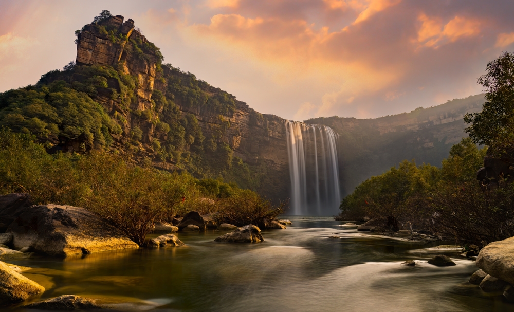  Lush greenery and a majestic waterfall cascading down a cliff, capturing the serene and tranquil natural environment reminiscent of Sayed Haider Raza's childhood in the village of Babaria, Madhya Pradesh.