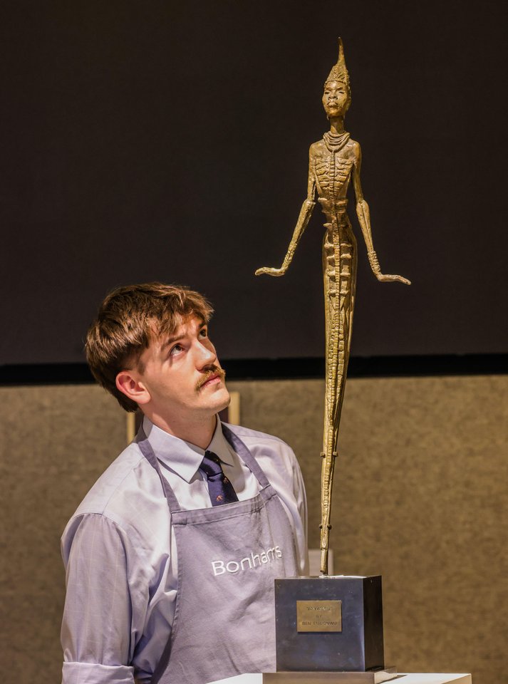 A Bonhams auction specialist stands beside Ben Enwonwu’s bronze sculpture “Anyanwu,” showcasing its elegant, elongated form and spiritual symbolism. | Aurora & Athena Auction House A Bonhams auction specialist stands beside Ben Enwonwu’s bronze sculpture “Anyanwu,” showcasing its elegant, elongated form and spiritual symbolism.