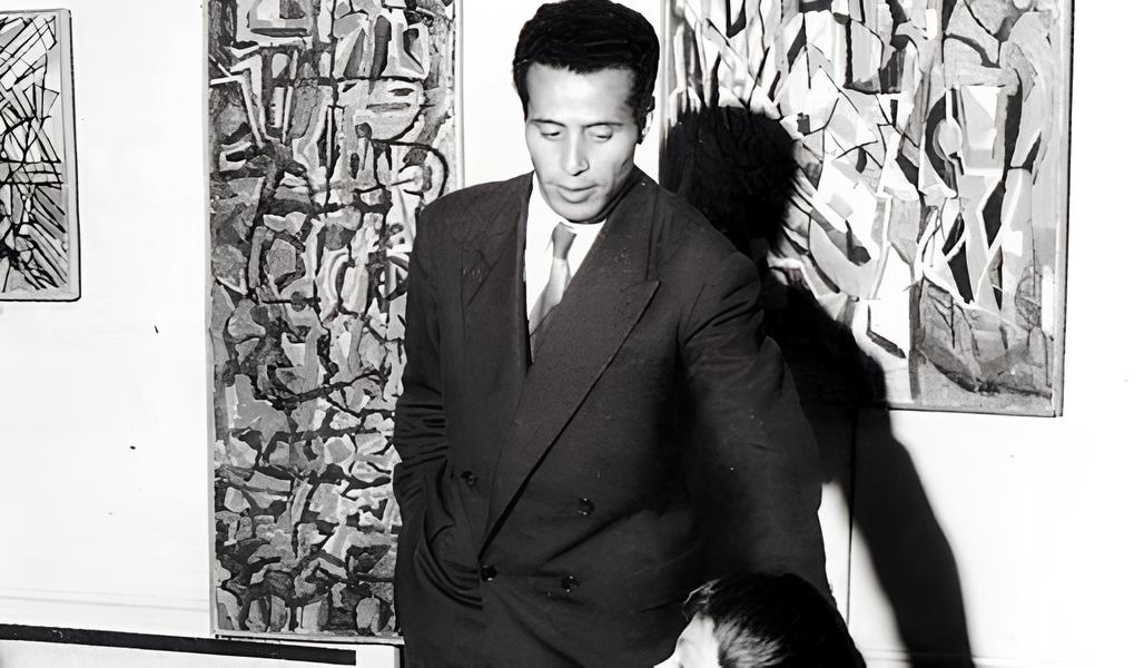 Black-and-white photograph of Moroccan abstract artist Jilali Gharbaoui in his Paris studio, circa 1960s, standing beside his gestural abstract paintings. | Aurora & Athena Auction House Black-and-white photograph of Moroccan abstract artist Jilali Gharbaoui in his Paris studio, circa 1960s, standing beside his gestural abstract paintings.